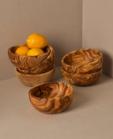 A set of natural olive wood bowls in various sizes, with the smallest bowls containing lemons. The bowls display a beautiful wood grain pattern.