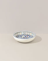 A ceramic hand painted decorative plate with a geometric pattern, predominantly white with blue and gold accents.