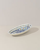 A hand painted decorative oval ceramic plate with a geometric pattern, predominantly white with blue and gold accents.