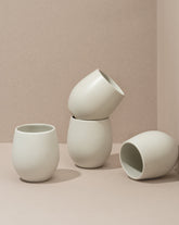 A set of four stoneware coffee cups arranged in a casual manner, with a matte white finish.