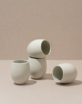 A set of four stoneware espresso tumblers in a neutral color, stacked in a pyramid shape against a neutral background.