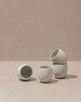 Four stoneware creamer cups in a matte finish, with one cup partially filled with a creamer, displayed against a neutral background.