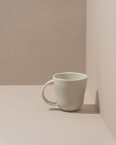 A white stoneware coffee mug placed against a neutral background.