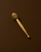 A natural olive wood honey spoon with a solid pattern, lying on a brown surface.