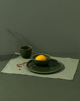 A green cotton placemat on a table with a plate and cup on top, against a dark background.