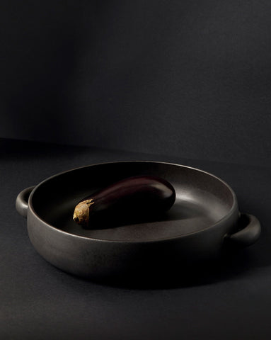 A white stoneware serving plate with handles, featuring a minimalist design, displayed with a piece of cauliflower on it, set against a neutral background.