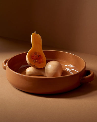 A white stoneware serving plate with handles, featuring a minimalist design, displayed with a piece of cauliflower on it, set against a neutral background.