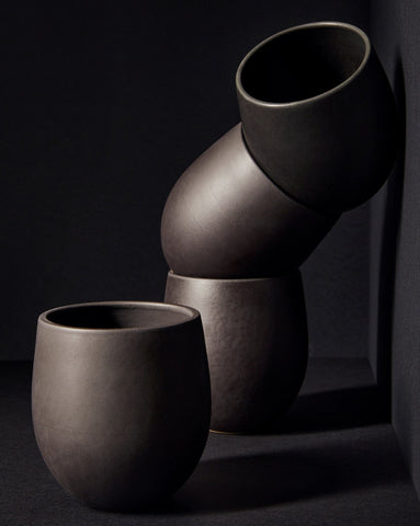 A set of beige stoneware coffee and tea cups with a matte finish, displayed in an artistic manner against a neutral background.