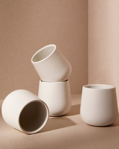 A set of three white stoneware coffee and tea cups of different sizes placed on a textured surface with a neutral background.
