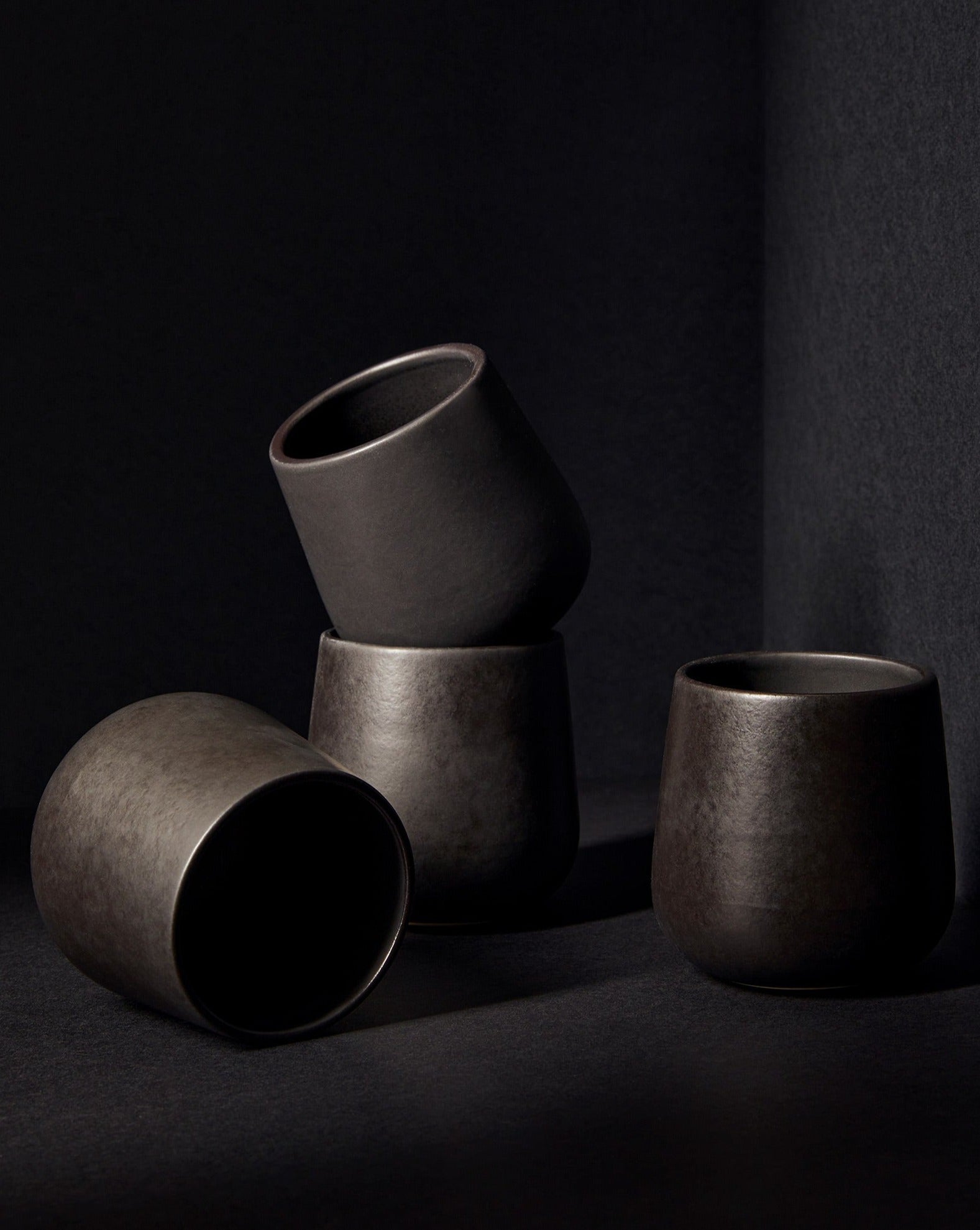 A set of three white stoneware coffee and tea cups of different sizes placed on a textured surface with a neutral background.