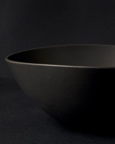Partially captured black stoneware serving bowl with the 'GHARYAN' logo visible, set against a black background.
