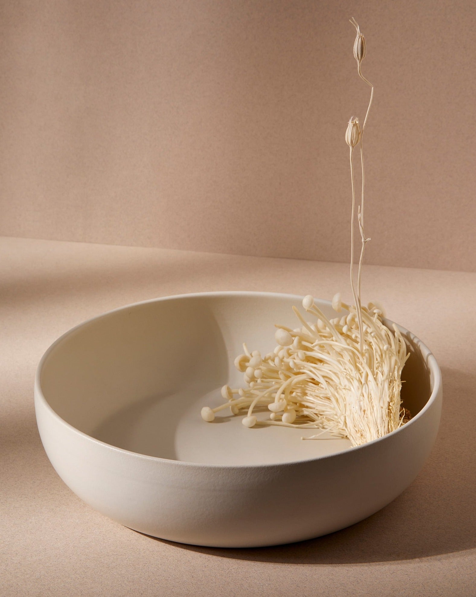 A beige Stoneware Shallow Serving Bowl with a capacity of 60 oz, displayed against a neutral background with a small amount of food items like pasta or noodles in it to showcase its size and shape.