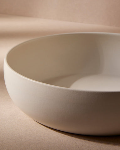 An empty off-white stoneware shallow serving bowl displayed against a plain white background, highlighting its soft, neutral tone and minimalist design.