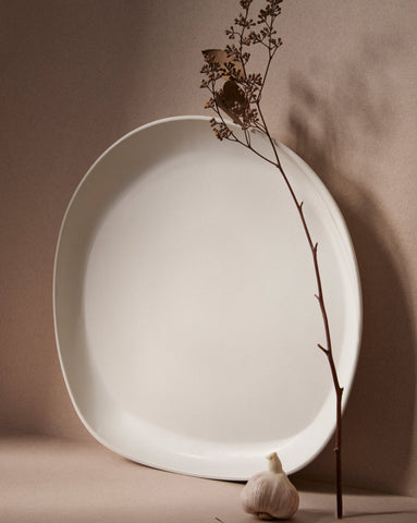 A stoneware serving platter with organic forms and a matte finish, presented on a table with food items arranged on top.