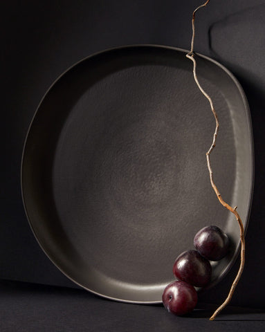 A stoneware serving platter with organic forms and a matte finish, presented on a table with food items arranged on top.