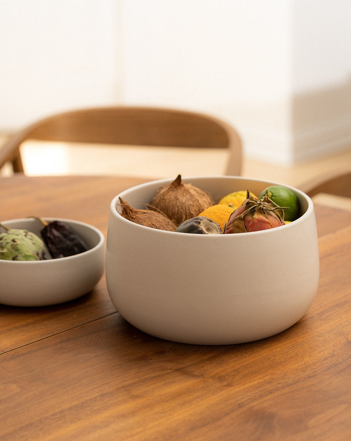 A large stoneware serving bowl in a neutral color, filled with assorted fruits on a wooden table.