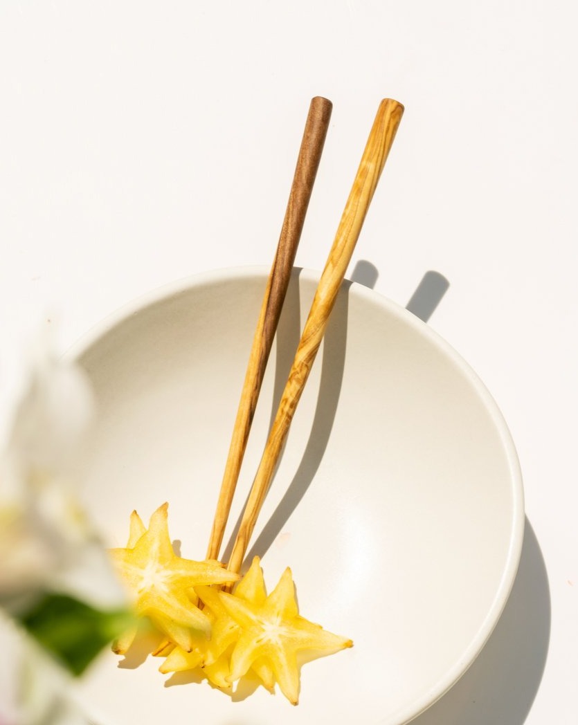 A pair of wooden chopsticks resting on a white bowl, with a star-shaped food item next to a flower.