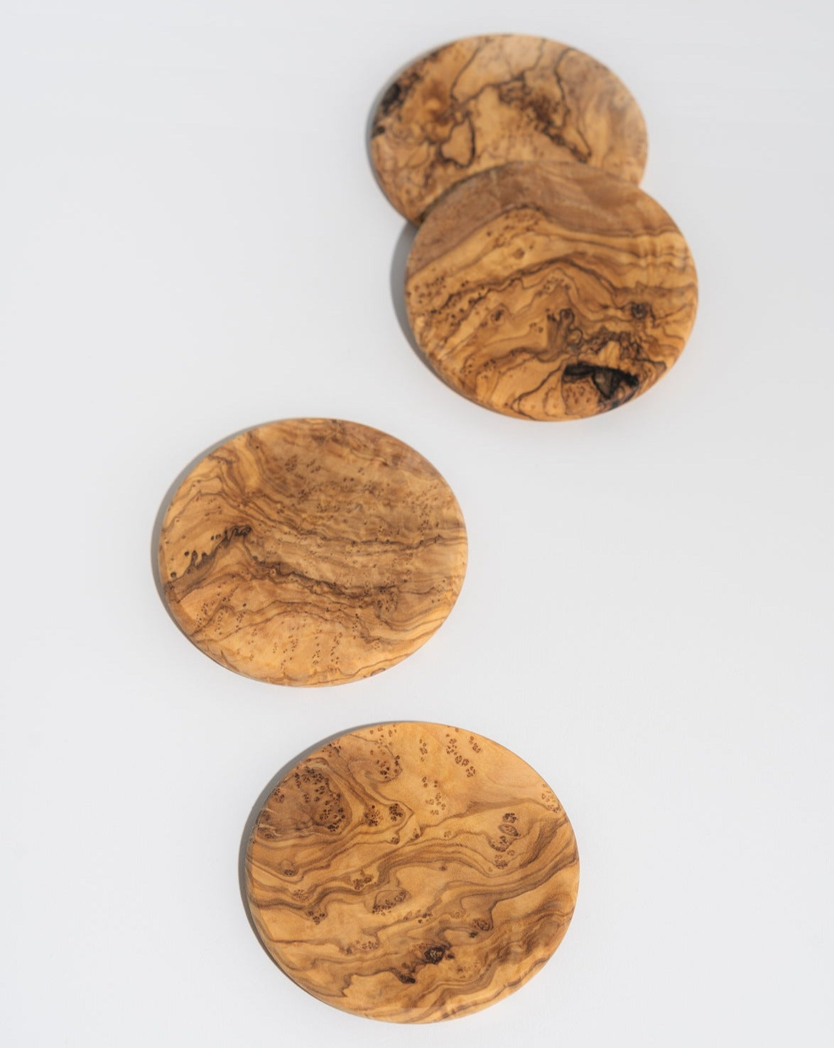 A set of four round olive wood coasters with natural grain patterns.