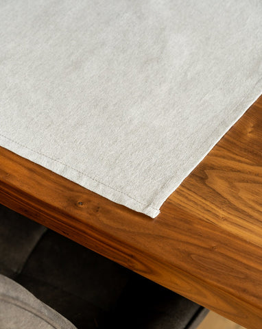 A Light grey cotton placemat is laid out on a wooden table.