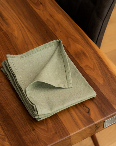 A folded Green cotton napkin on a wooden dining table