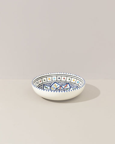 A ceramic hand painted decorative plate with a geometric pattern, predominantly white with blue and gold accents.