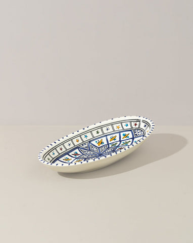 A hand painted decorative oval ceramic plate with a geometric pattern, predominantly white with blue and gold accents.