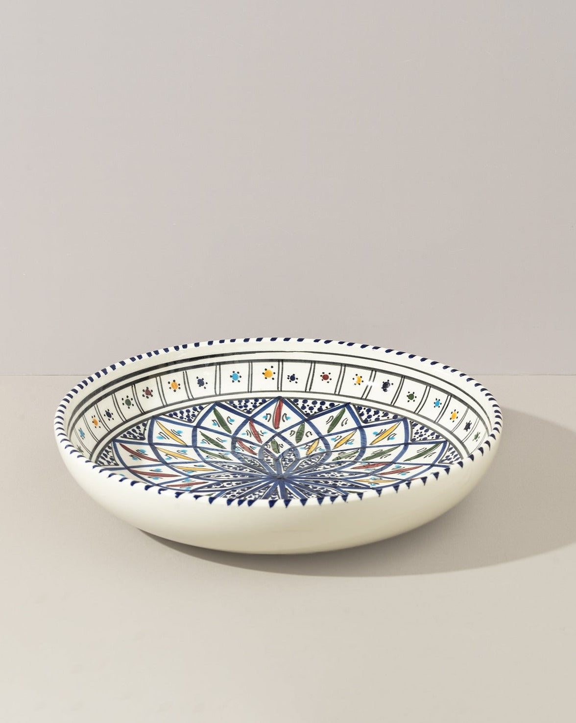 A ceramic decorative large bowl with hand-painted patterns in blue, green, and other colors on a white background, displayed against a neutral backdrop.