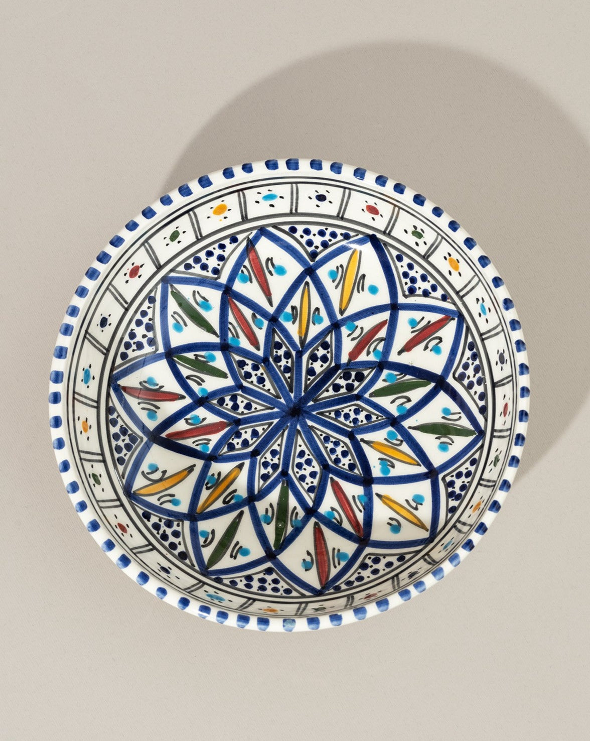 A ceramic hand painted decorative plate with a geometric pattern, predominantly white with blue and gold accents.