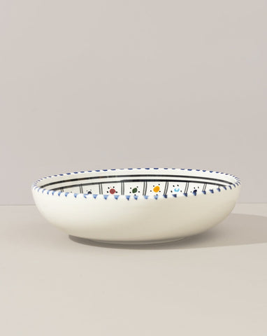 A ceramic hand painted decorative plate with a geometric pattern, predominantly white with blue and gold accents.