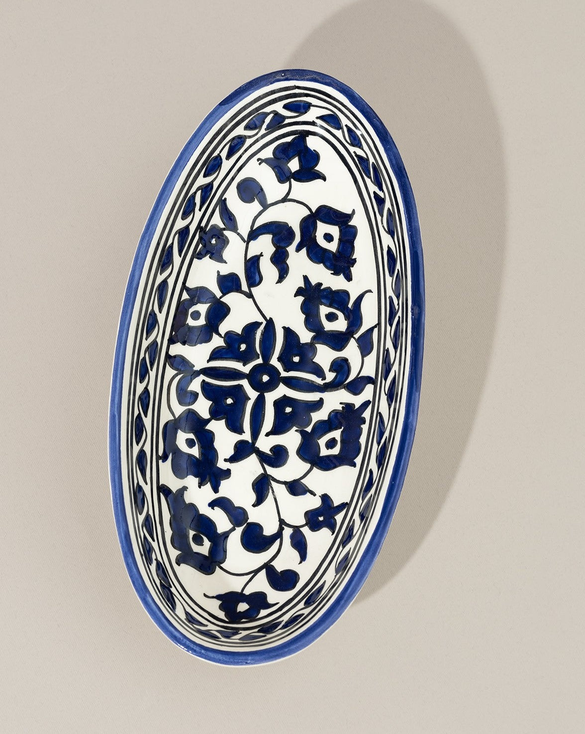 A single oval ceramic plate with a hand-painted blue and white floral design, displayed on a white background, highlighting its delicate craftsmanship.
