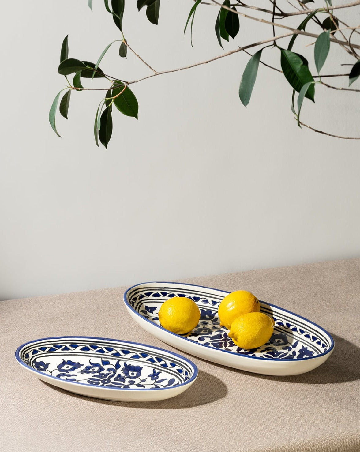 Two oval ceramic plates with a hand-painted floral design in blue and white, displayed on a neutral background with lemons on top.