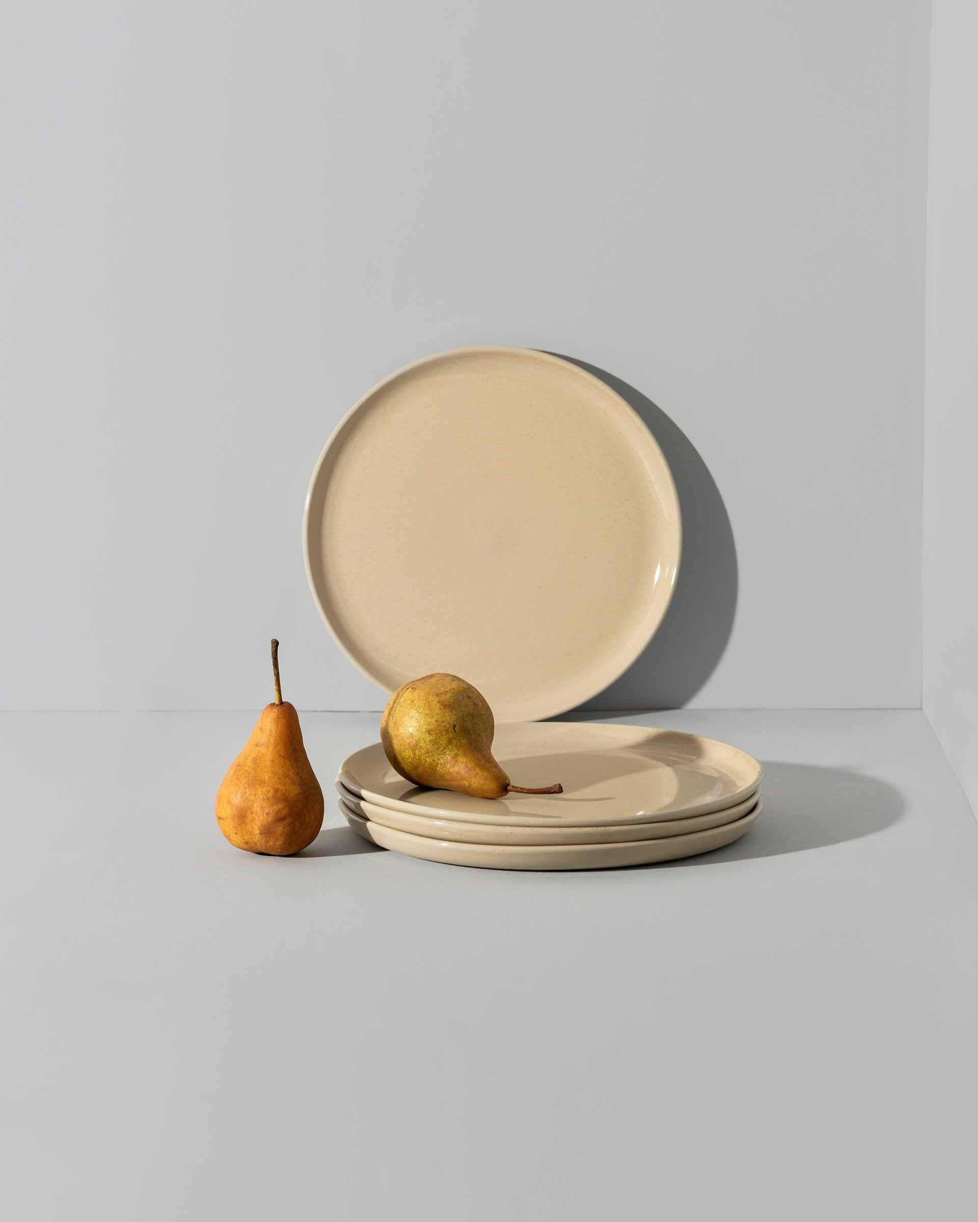 Two stoneware flat plates with a matte finish, one with a plain beige surface and the other with a beige edge and white interior.