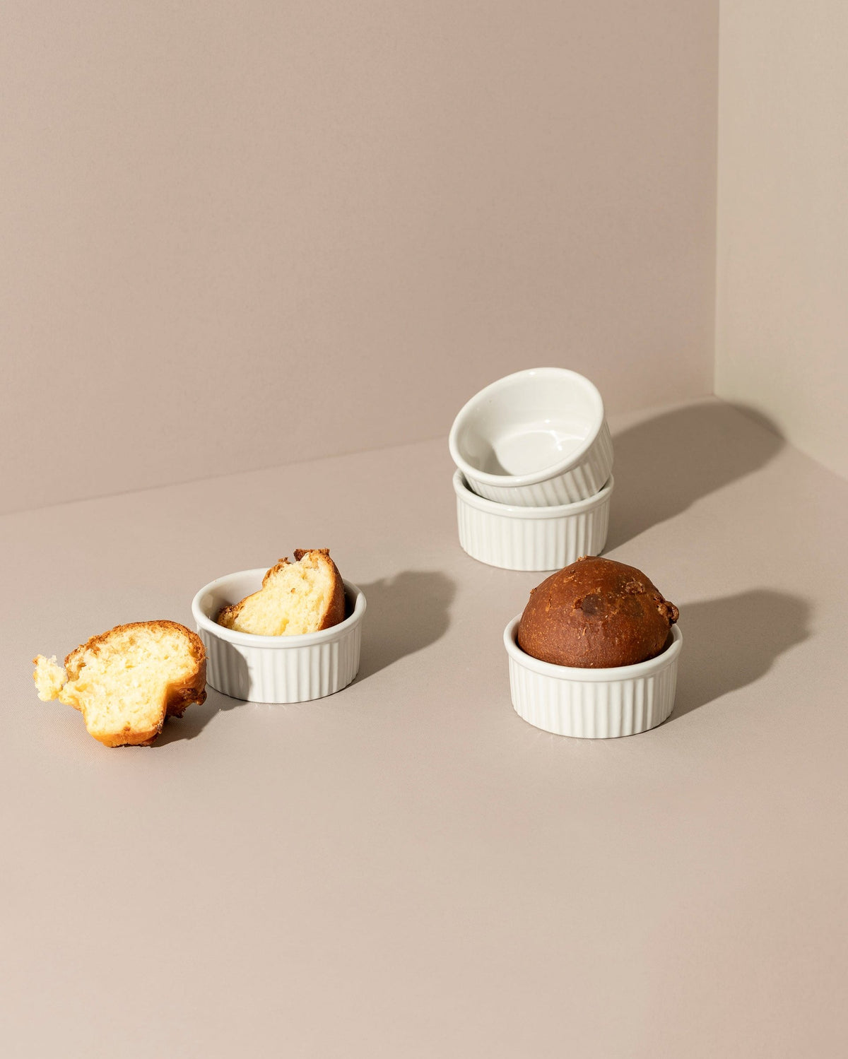 Three stoneware ramekins of varying sizes with lids, displayed on a neutral background. One ramekin contains a baked dessert, possibly a soufflé, and the other two are empty.