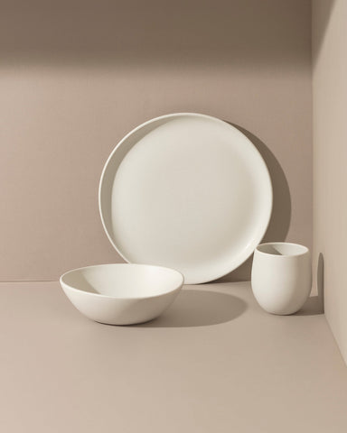 A set of white stoneware dinnerware including a flat salad plate, a dinner bowl, and a mug.
