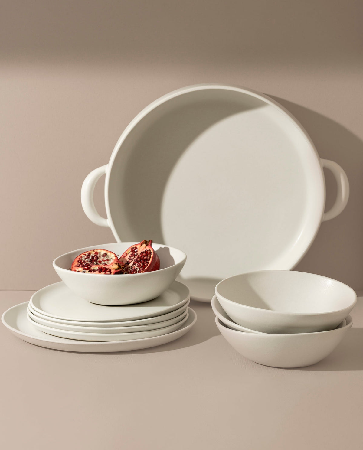 A set of white stoneware dinnerware including flat round dinner plates, flat round salad plates, organic-shaped soup bowls, and a large plate with handles.