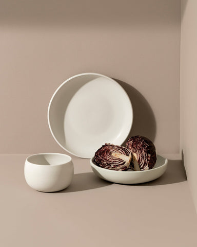 A set of white stoneware dinnerware on a neutral background, including bowls and plates.