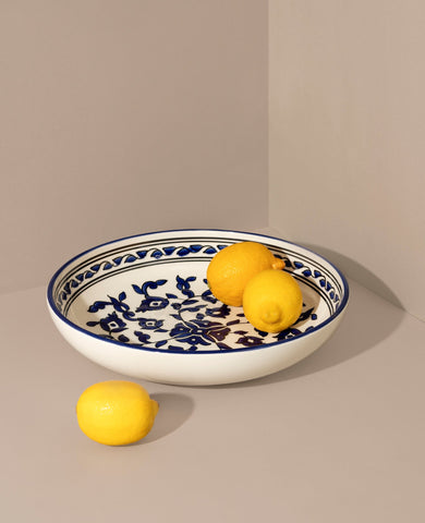 A hand-painted ceramic decorative bowl with a floral and blue pattern, featuring a lemon design on the side, placed on a neutral background.