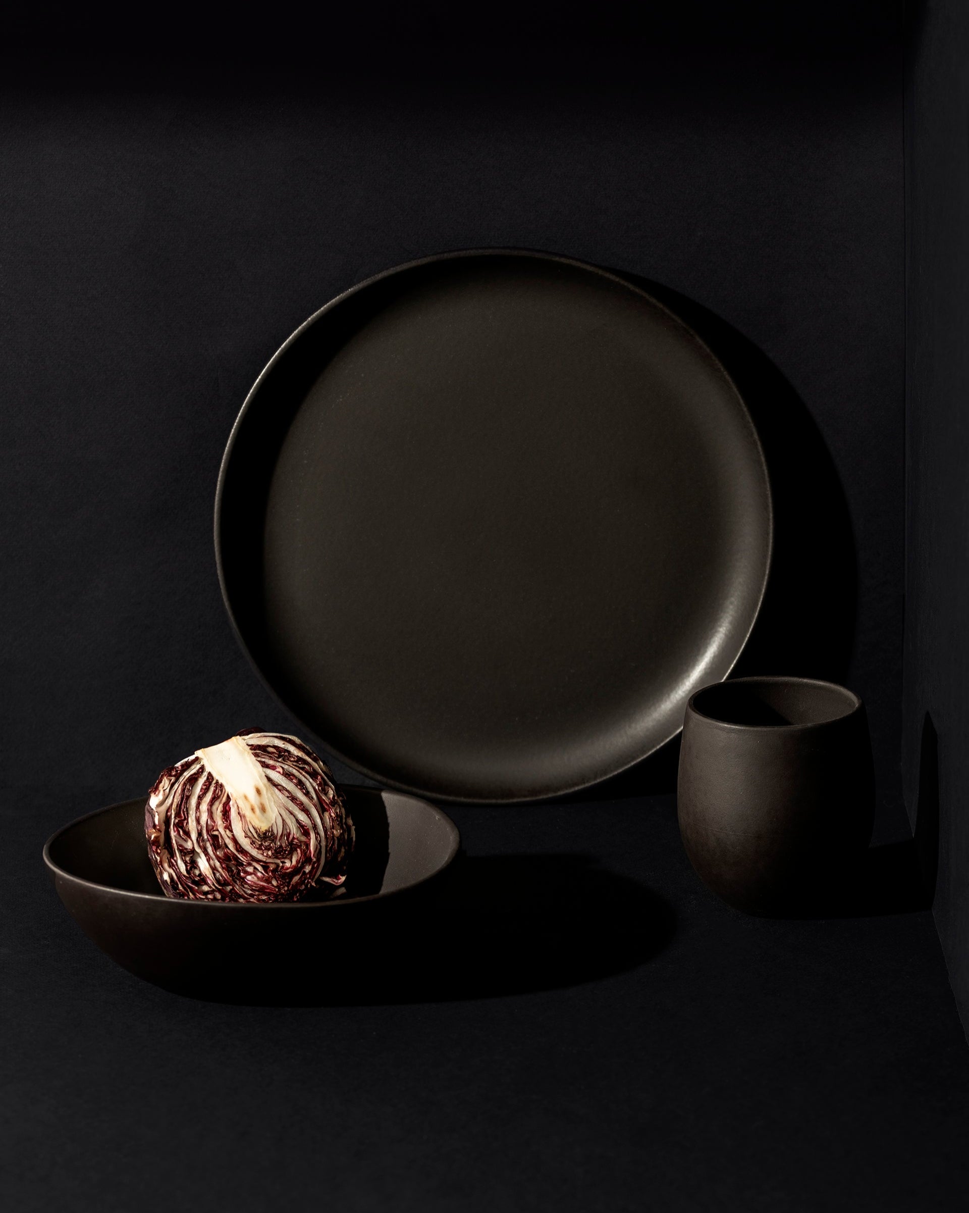 A set of white stoneware dinnerware including a flat salad plate, a dinner bowl, and a mug.
