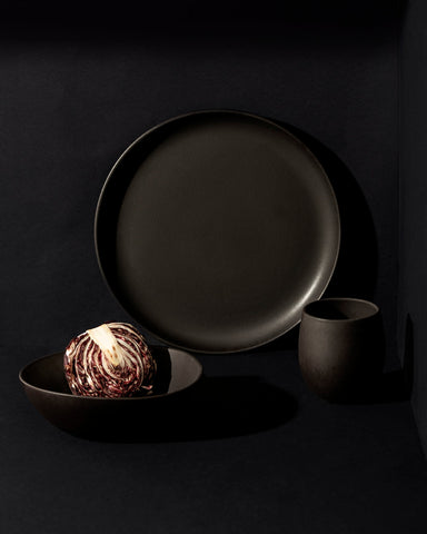 A set of white stoneware dinnerware including a flat salad plate, a dinner bowl, and a mug.