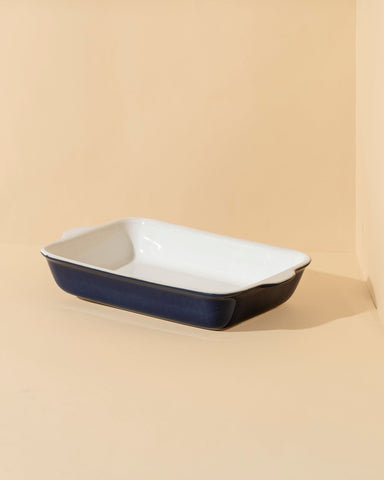 A stack of rectangular stoneware baking dishes in beige, blue, and green colors.