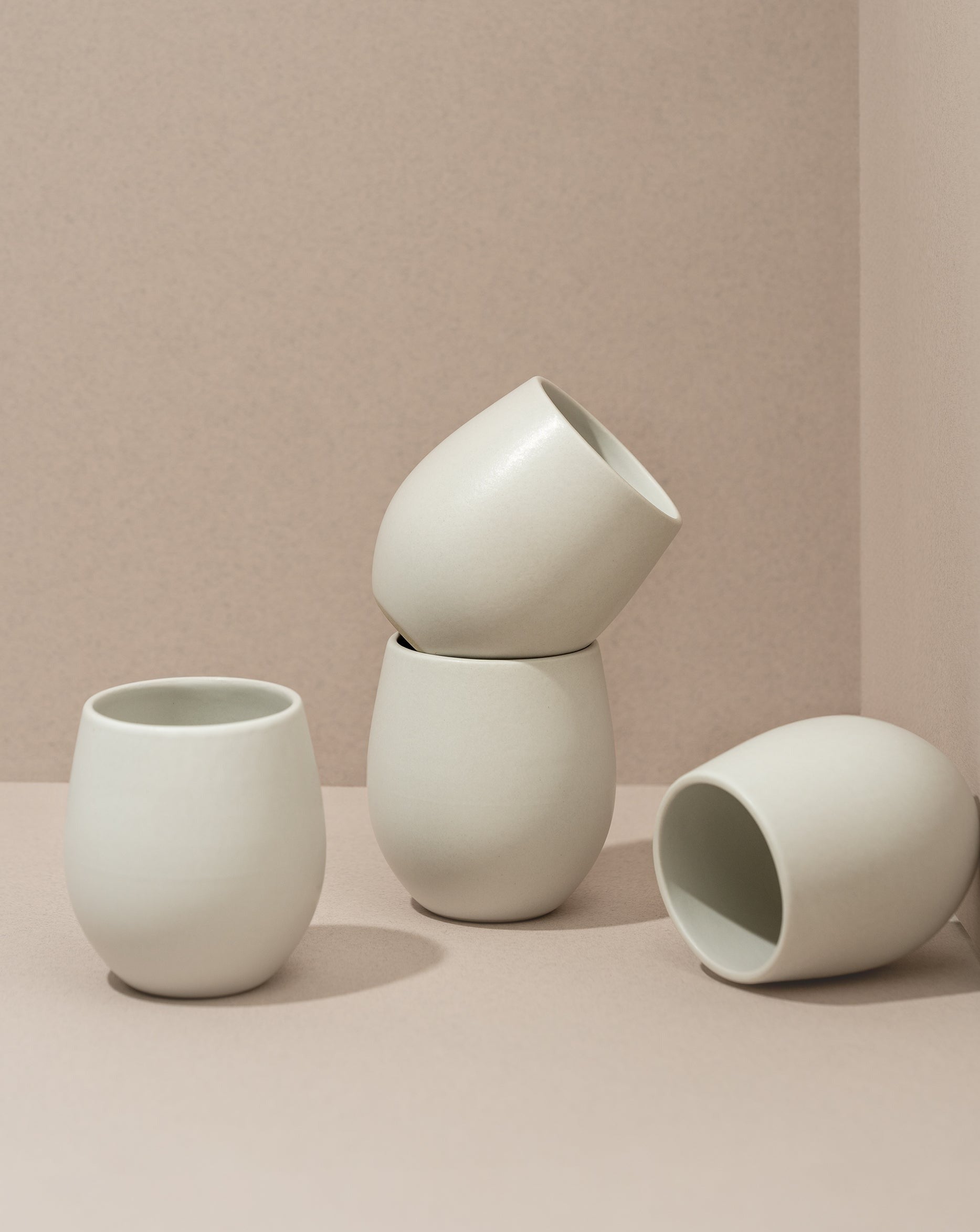 A set of four stoneware coffee cups arranged in a casual manner, with a matte white finish.
