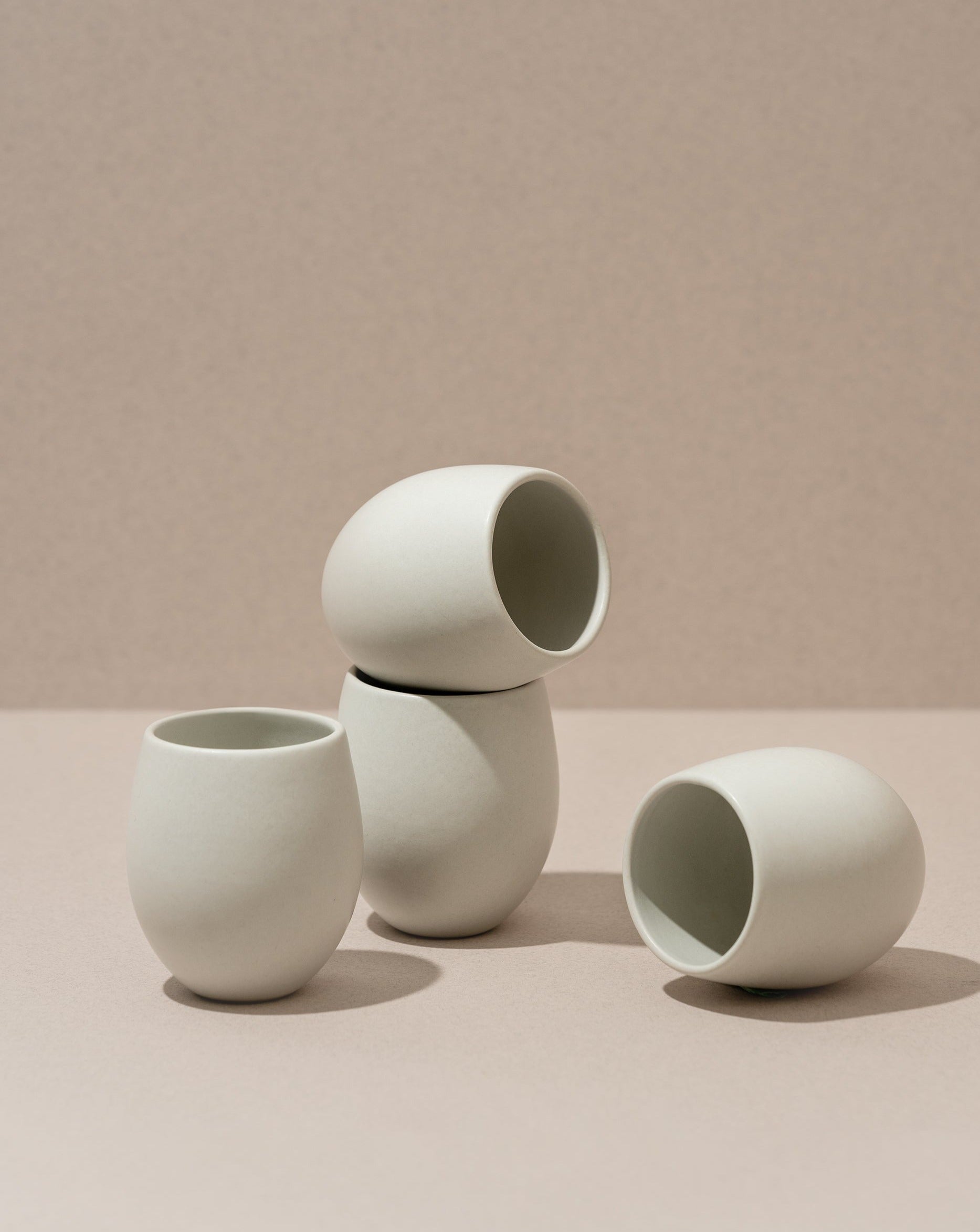 A set of four stoneware espresso tumblers in a neutral color, stacked in a pyramid shape against a neutral background.