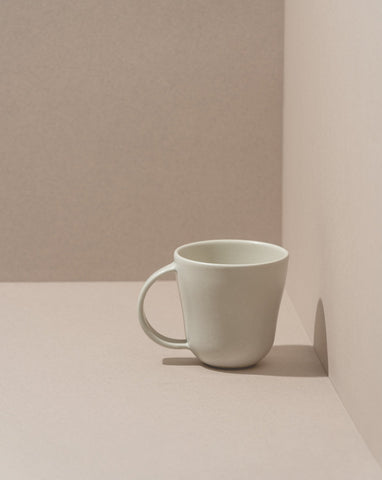 A white stoneware coffee mug placed against a neutral background.