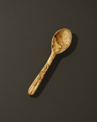 A natural olive wood kitchen spoon on a dark background.
