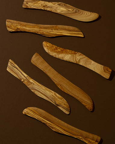 A wooden butter spreader with a curved handle, laying on a brown surface.