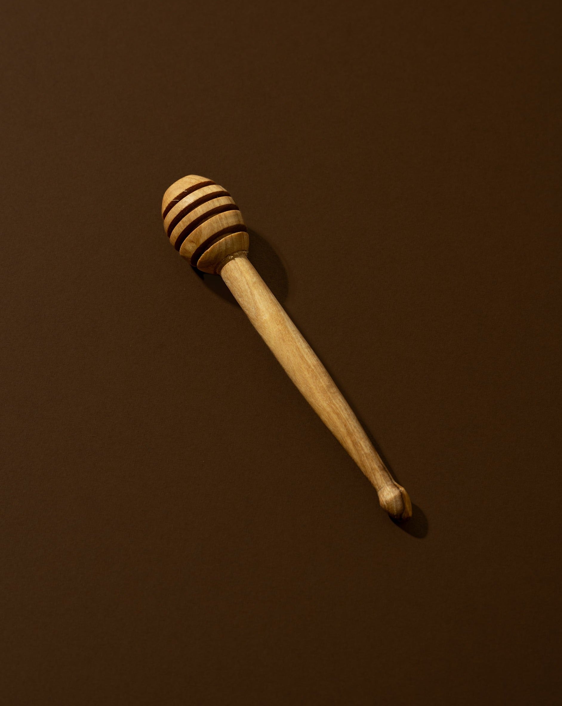 A natural olive wood honey spoon with a solid pattern, lying on a brown surface.