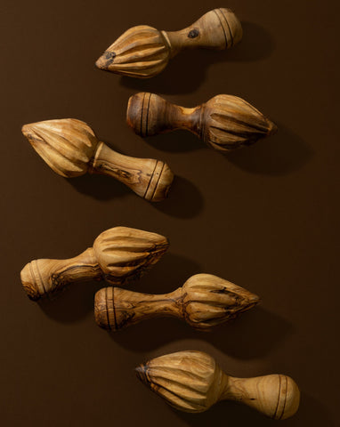 A set of wooden lemon press with natural olive wood patterns, lying on a brown surface.