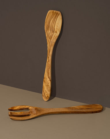 A wooden spoon and fork set made of olivewood, displayed against a dark background.