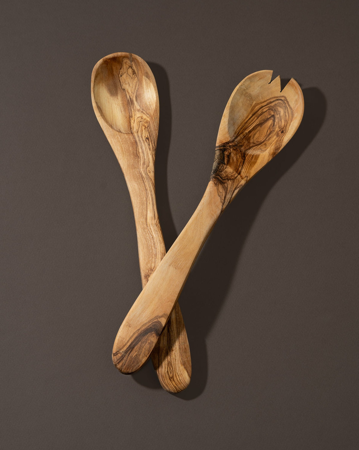 A pair of olive wood utensils, likely a spoon and fork, laid on a dark surface.