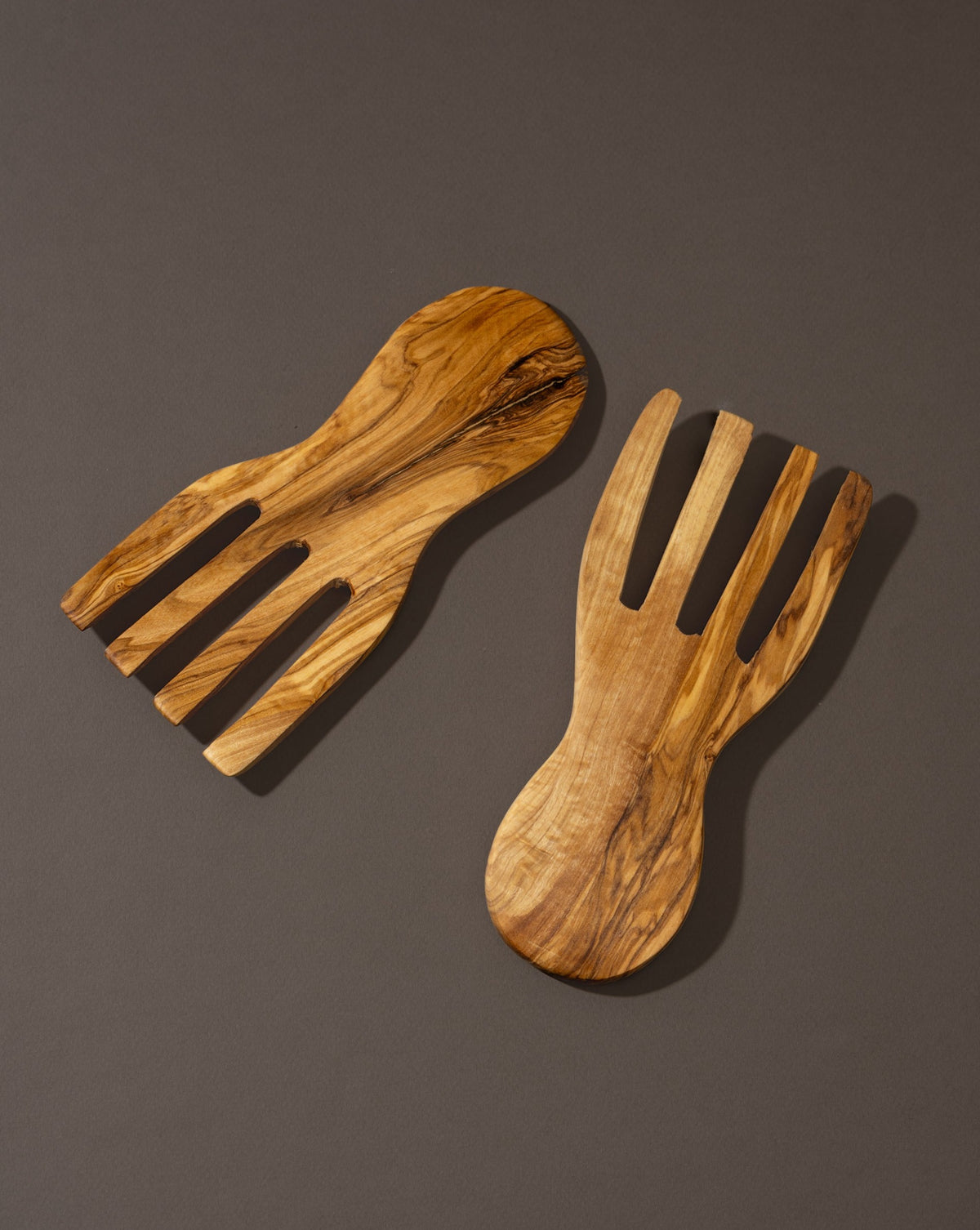 A pair of flat olivewood serving forks placed on a dark surface.